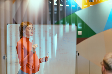 Image showing A pregnant business woman with orange hair confidently presents her business plan to colleagues in a modern glass office, embodying entrepreneurship and innovation