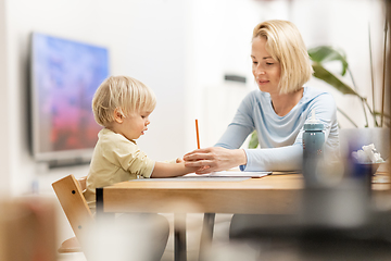 Image showing Caring young Caucasian mother and small son drawing painting in notebook at home together. Loving mom or nanny having fun learning and playing with her little 1,5 year old infant baby boy child.