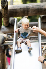 Image showing Parent hand holding little infant baby boy child while sliding on urban playground on a sunny summer day. Family joy and happiness concept