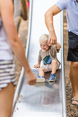 Image showing Parent hand holding little infant baby boy child while sliding on urban playground on a sunny summer day. Family joy and happiness concept