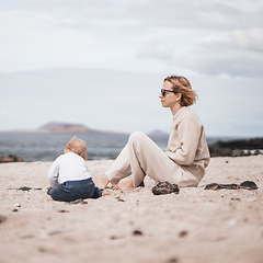 Image showing Mother enjoying winter beach vacations playing with his infant baby boy son on wild volcanic sandy beach on Lanzarote island, Canary Islands, Spain. Family travel and vacations concept