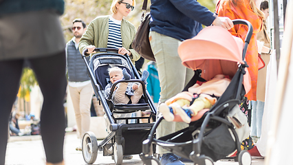 Image showing Mother walking and pushing his infant baby boy child in stroller in crowd of people wisiting sunday flea market in Malaga, Spain.