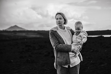 Image showing Mother enjoying winter vacations playing with his infant baby boy son on black sandy volcanic beach of Janubio on Lanzarote island, Spain on windy overcast day. Family travel vacations concept.