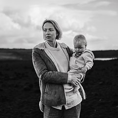 Image showing Mother enjoying winter vacations playing with his infant baby boy son on black sandy volcanic beach of Janubio on Lanzarote island, Spain on windy overcast day. Family travel vacations concept.