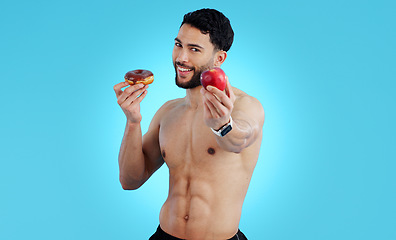 Image showing Happy man, portrait and apple with donut for diet, health or nutrition against a blue studio background. Male person or athlete showing natural organic red fruit with chocolate desert on mockup space
