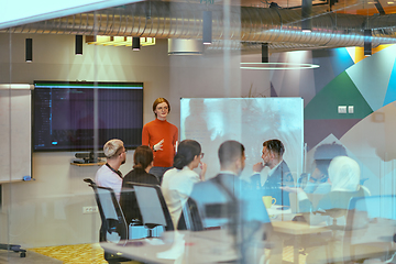 Image showing A pregnant business woman with orange hair confidently presents her business plan to colleagues in a modern glass office, embodying entrepreneurship and innovation