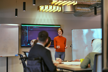 Image showing A pregnant business woman with orange hair confidently presents her business plan to colleagues in a modern glass office, embodying entrepreneurship and innovation