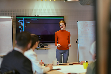 Image showing A pregnant business woman with orange hair confidently presents her business plan to colleagues in a modern glass office, embodying entrepreneurship and innovation