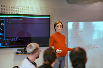 Image showing A pregnant business woman with orange hair confidently presents her business plan to colleagues in a modern glass office, embodying entrepreneurship and innovation