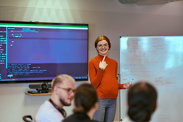 Image showing A pregnant business woman with orange hair confidently presents her business plan to colleagues in a modern glass office, embodying entrepreneurship and innovation