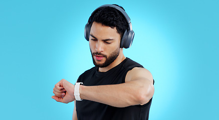 Image showing Man, headphones and checking watch in fitness for performance against a blue studio background. Male person, athlete or model looking at wristwatch for monitoring or tracking steps on mockup space