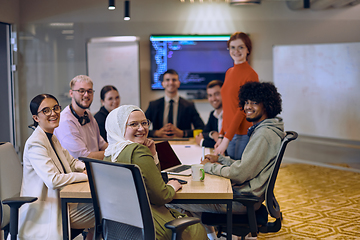 Image showing A diverse team of business experts in a modern glass office, attentively listening to a colleague's presentation, fostering collaboration and innovation.