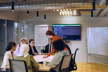 Image showing A diverse team of business experts in a modern glass office, attentively listening to a colleague's presentation, fostering collaboration and innovation.