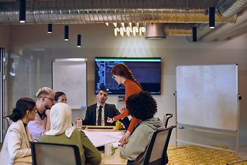 Image showing A diverse team of business experts in a modern glass office, attentively listening to a colleague's presentation, fostering collaboration and innovation.