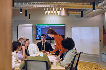 Image showing A diverse team of business experts in a modern glass office, attentively listening to a colleague's presentation, fostering collaboration and innovation.