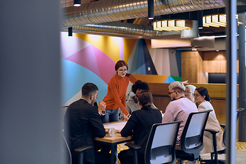 Image showing A diverse team of business experts in a modern glass office, attentively listening to a colleague's presentation, fostering collaboration and innovation.