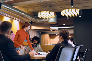 Image showing A diverse team of business experts in a modern glass office, attentively listening to a colleague's presentation, fostering collaboration and innovation.