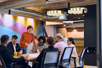 Image showing A diverse team of business experts in a modern glass office, attentively listening to a colleague's presentation, fostering collaboration and innovation.