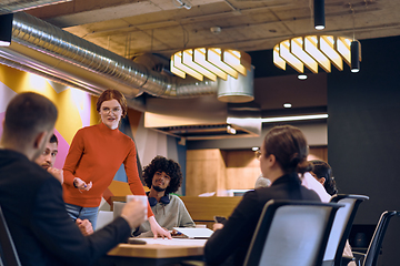 Image showing A diverse team of business experts in a modern glass office, attentively listening to a colleague's presentation, fostering collaboration and innovation.