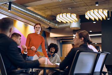 Image showing A diverse team of business experts in a modern glass office, attentively listening to a colleague's presentation, fostering collaboration and innovation.