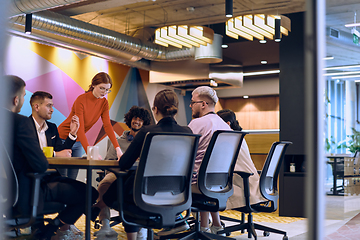 Image showing A diverse team of business experts in a modern glass office, attentively listening to a colleague's presentation, fostering collaboration and innovation.