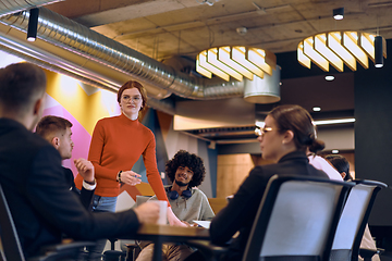 Image showing A diverse team of business experts in a modern glass office, attentively listening to a colleague's presentation, fostering collaboration and innovation.