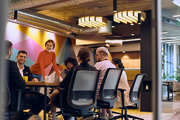 Image showing A diverse team of business experts in a modern glass office, attentively listening to a colleague's presentation, fostering collaboration and innovation.