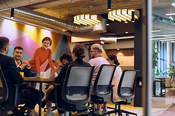 Image showing A diverse team of business experts in a modern glass office, attentively listening to a colleague's presentation, fostering collaboration and innovation.