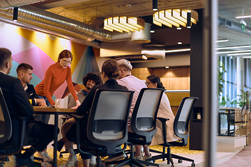 Image showing A diverse team of business experts in a modern glass office, attentively listening to a colleague's presentation, fostering collaboration and innovation.