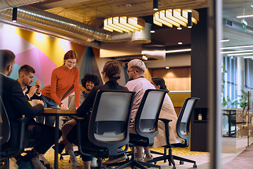 Image showing A diverse team of business experts in a modern glass office, attentively listening to a colleague's presentation, fostering collaboration and innovation.