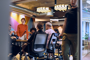 Image showing A diverse team of business experts in a modern glass office, attentively listening to a colleague's presentation, fostering collaboration and innovation.