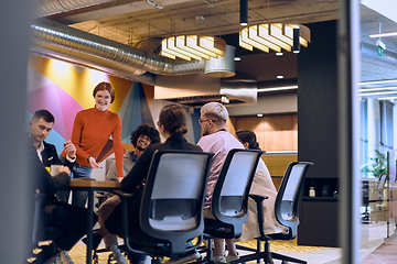 Image showing A diverse team of business experts in a modern glass office, attentively listening to a colleague's presentation, fostering collaboration and innovation.