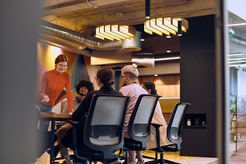 Image showing A diverse team of business experts in a modern glass office, attentively listening to a colleague's presentation, fostering collaboration and innovation.