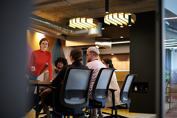 Image showing A diverse team of business experts in a modern glass office, attentively listening to a colleague's presentation, fostering collaboration and innovation.