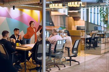 Image showing A diverse team of business experts in a modern glass office, attentively listening to a colleague's presentation, fostering collaboration and innovation.