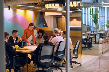 Image showing A diverse team of business experts in a modern glass office, attentively listening to a colleague's presentation, fostering collaboration and innovation.