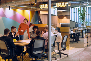 Image showing A diverse team of business experts in a modern glass office, attentively listening to a colleague's presentation, fostering collaboration and innovation.