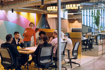 Image showing A diverse team of business experts in a modern glass office, attentively listening to a colleague's presentation, fostering collaboration and innovation.