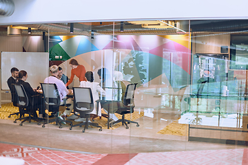 Image showing A diverse team of business experts in a modern glass office, attentively listening to a colleague's presentation, fostering collaboration and innovation.