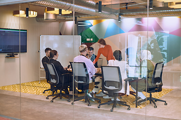 Image showing A diverse team of business experts in a modern glass office, attentively listening to a colleague's presentation, fostering collaboration and innovation.