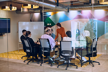 Image showing A diverse team of business experts in a modern glass office, attentively listening to a colleague's presentation, fostering collaboration and innovation.