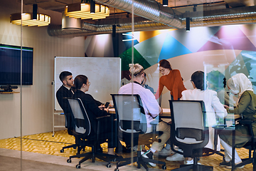 Image showing A diverse team of business experts in a modern glass office, attentively listening to a colleague's presentation, fostering collaboration and innovation.