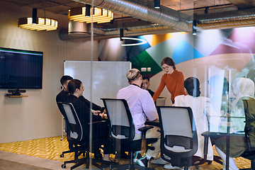 Image showing A diverse team of business experts in a modern glass office, attentively listening to a colleague's presentation, fostering collaboration and innovation.