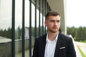 Image showing A CEO dressed in a sleek black suit stands confidently at the entrance of a modern corporate building, awaiting the start of the workday in the bustling urban environment.