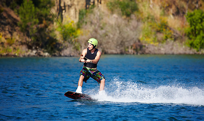 Image showing Man, wakeboarding and water with helmet, sport and fitness for speed on vacation in summer sunshine. Person, athlete and ski with rope for safety on lake, sea or river for training, exercise or waves