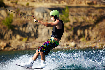 Image showing Man, wakeboarding outdoor and water with helmet, sport and fitness for speed in summer sunshine. Person, athlete and ski with rope for safety on lake, sea or river for training, exercise and waves