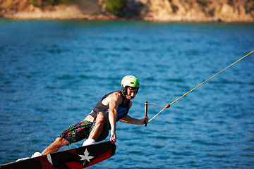 Image showing Man, wakeboarding outdoor and lake with helmet, sport and fitness for speed in summer sunshine. Person, athlete and ski with rope for safety on water, sea or river for training, exercise and freedom