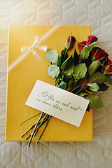 Image showing Box, roses and letter on bed, gift and invitation in closeup, above or message for valentines day in hotel. Flowers, bouquet or plants with cardboard package, notes or clothes in bedroom in home