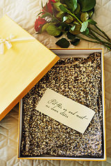 Image showing Box, flowers and invitation paper on bed, gift or dress in closeup, above or message on valentines day in hotel. Roses, bouquet or fashion in cardboard package, notes and letter in bedroom in home