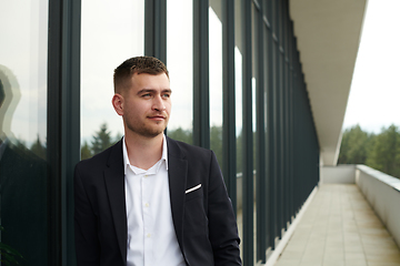 Image showing A CEO dressed in a sleek black suit stands confidently at the entrance of a modern corporate building, awaiting the start of the workday in the bustling urban environment.